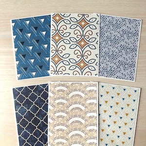 May include: Six decorative cards with various geometric patterns. Designs include blue triangles, mosaic-style swirls, and arched tile patterns in shades of blue, brown, and beige. The cards are arranged on a light wood surface.