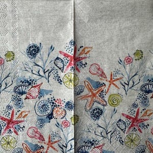 May include: A white fabric napkin with a repeating pattern of blue, red, and orange starfish and seashells. The background is a light gray with a subtle texture.