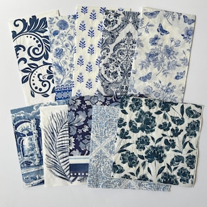 May include: A collection of paper napkins with various blue and white patterns. Designs include floral, botanical, and damask motifs. Some napkins feature butterflies and architectural scenes. The napkins are arranged on a white surface.