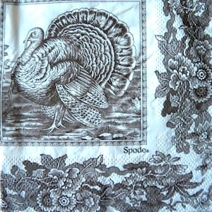 May include: A white and brown napkin with a detailed illustration of a turkey with its feathers fanned out. The napkin has a decorative floral border and the brand name "Spode" is visible.