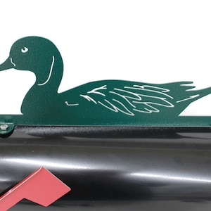 May include: Green metal duck mailbox topper. The duck is in a swimming position with its head turned to the side. The mailbox topper is attached to a black mailbox.