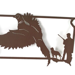 May include: A brown metal wall art piece depicting a pheasant in flight, a hunter with a rifle, and a dog. The artwork is in the shape of a state outline, with a rectangular border.