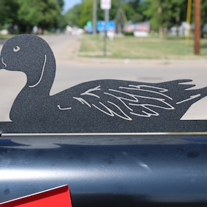May include: A black metal silhouette of a duck, mounted on a black mailbox. The duck is facing left and has a detailed design.