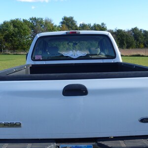 May include: White pickup truck with a black bed and a rear window sticker that says "F-250 Super Duty".