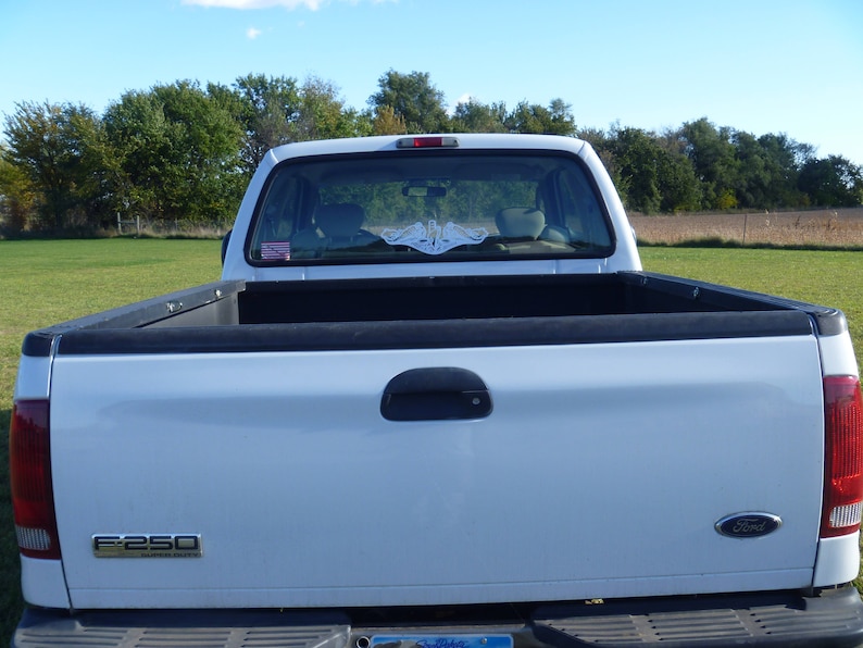 May include: White pickup truck with a black bed and a rear window sticker that says "F-250 Super Duty".