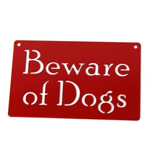 May include: Red metal sign with white lettering that reads "Beware of Dogs".