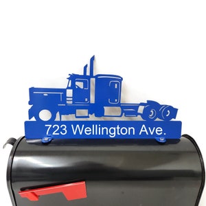 May include: A blue metal truck-shaped mailbox topper with the address "723 Wellington Ave." in white. The topper is mounted on a black mailbox with a red flag.