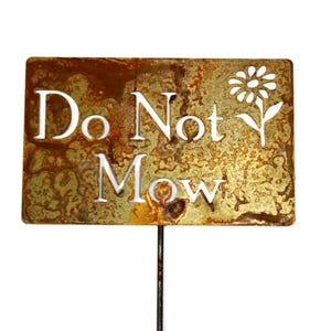 May include: A rectangular metal garden sign with the words "Do Not Mow" cut out in white. The sign has a flower design and is mounted on a metal stake. The sign has a rustic, weathered appearance.