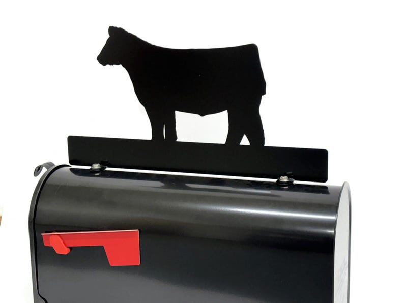 May include: A black mailbox with a red flag and a black cow silhouette on top. The mailbox has a standard shape and size, with a glossy finish. The cow silhouette is a simple design.