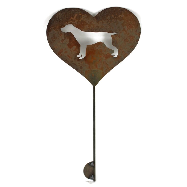 May include: A heart-shaped, rusty metal garden stake featuring a cut-out silhouette of a dog. The stake has a long, thin stem and a small, rounded base for easy placement in the garden. The dog silhouette is a light color.
