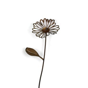 May include: A metal daisy sculpture with a brown stem, leaf, and flower. The flower has a circular center and thin, curved petals. The leaf is oval-shaped. The sculpture is set against a white background.