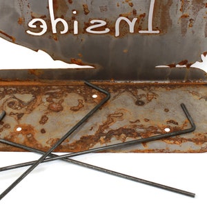 May include: A rusty metal fire pit with a cutout design of a tree and the word "Inside" written on it. The fire pit has a metal grate and comes with three metal rods for supporting the grate.