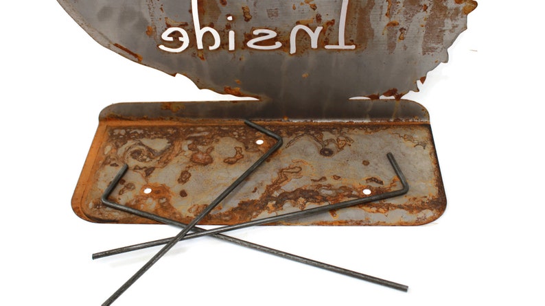 May include: A rusty metal fire pit with a cutout design of a tree and the word "Inside" written on it. The fire pit has a metal grate and comes with three metal rods for supporting the grate.
