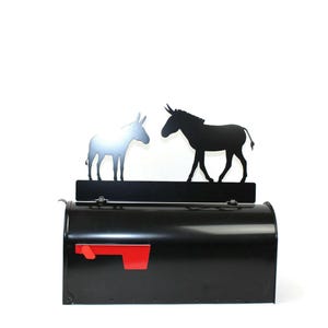 Puede incluir: Buz&oacute;n negro con una bandera roja y una silueta met&aacute;lica de dos burros enfrentados en la parte superior.