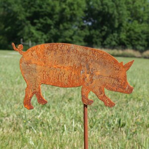 May include: A rusty metal pig silhouette garden stake. The pig is facing right and has a curled tail. The stake is inserted into the ground.