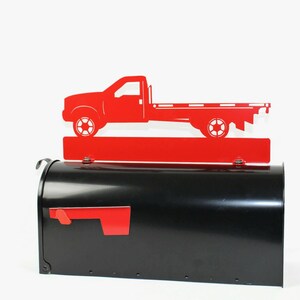 Pode incluir: Tope de caixa de correio de metal vermelho com a silhueta de um caminh&atilde;o de plataforma. O topo da caixa de correio est&aacute; montado em uma caixa de correio preta.