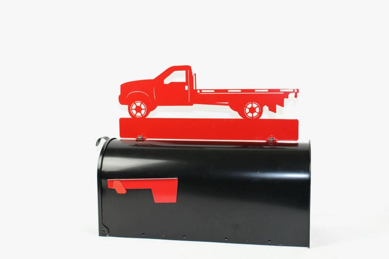 Pode incluir: Tope de caixa de correio de metal vermelho com a silhueta de um caminh&atilde;o de plataforma. O topo da caixa de correio est&aacute; montado em uma caixa de correio preta.