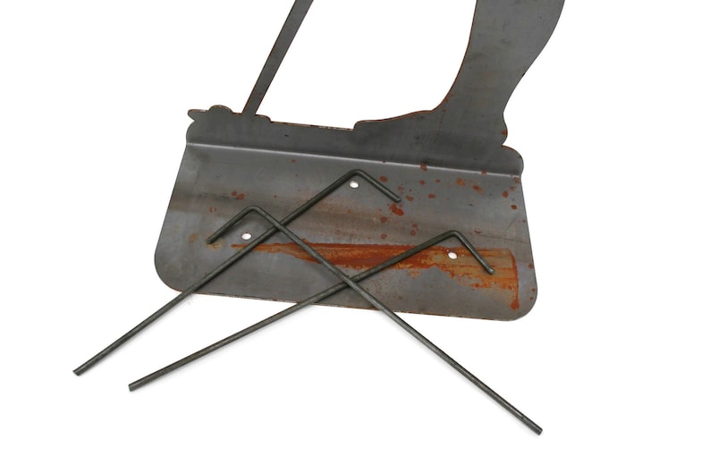 May include: A weathered metal garden stake featuring a silhouette of a person with a bag, along with three metal stakes. The metal has a rusty appearance, suggesting outdoor use. The design is simple and functional.