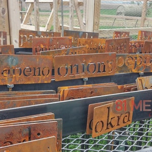 May include: A collection of weathered, rusty metal garden markers with cut-out lettering. The markers are labeled with various garden vegetables and herbs, including "jalapeno" and "onions". The image also shows the text "81 METAL".