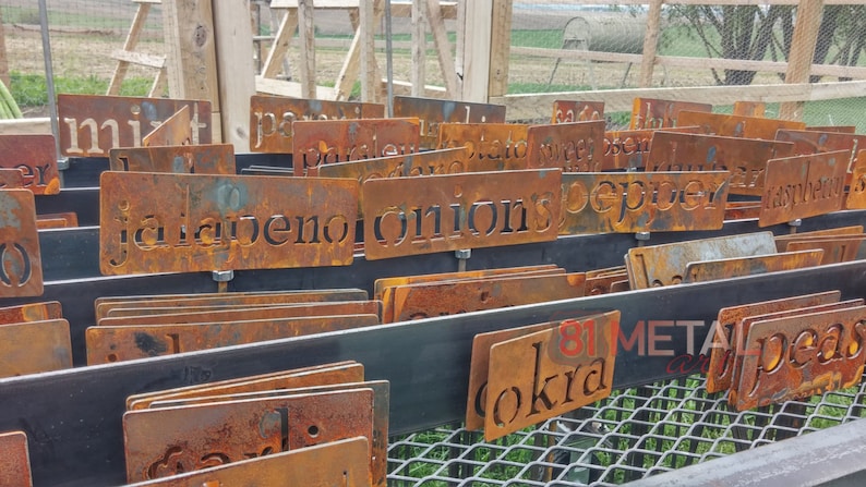 May include: A collection of weathered, rusty metal garden markers with cut-out lettering. The markers are labeled with various garden vegetables and herbs, including "jalapeno" and "onions". The image also shows the text "81 METAL".