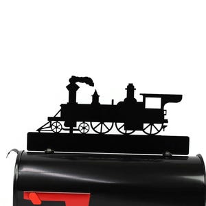 May include: Black metal train silhouette mailbox topper. The topper features a detailed outline of a classic steam engine with smoke billowing from the smokestack. The mailbox is black with a red flag.