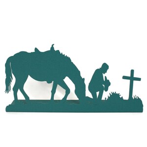 May include: Teal metal silhouette depicting a horse grazing, a person kneeling in prayer, and a cross. The artwork is a single piece, suitable for wall decor or as a decorative accent. The design evokes themes of faith and the outdoors.