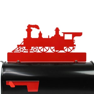May include: A red metal train silhouette decorates a black mailbox. The train is a classic steam engine design, with a smokestack and multiple wheels. The mailbox has a red flag and a curved handle.