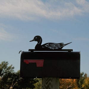 May include: Black metal mailbox with a duck silhouette on top. The mailbox is mounted on a wooden post.