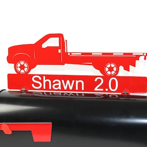 Pode incluir: Tope de caixa de correio de metal vermelho com uma silhueta de caminhonete vermelha e o nome "Shawn 2.0" em um fundo branco.