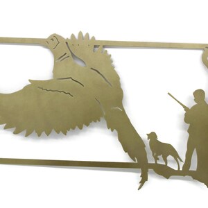 May include: A brass-colored metal wall art piece depicting a pheasant in flight, a hunter with a rifle, and a dog, all within the outline of a state. The artwork is a silhouette style.