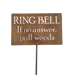 May include: A rectangular, weathered metal sign with the words "RING BELL" at the top, followed by "If no answer, pull weeds" in a serif font. The sign is mounted on a thin metal stake, perfect for a garden.