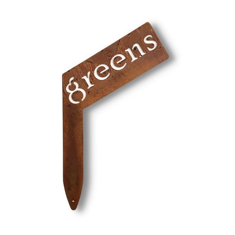 May include: A rusty metal garden marker with the word "Greens" cut out in white. The marker is shaped like a right angle and has a pointed end for inserting into the ground.