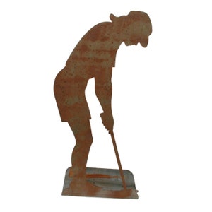 May include: A rusty metal silhouette of a golfer in a putting stance. The figure is bent over, holding a golf club, with a hat and shorts. The base is a rectangular shape. The metal has a weathered, textured appearance.