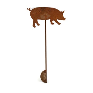 May include: A rusty metal pig silhouette mounted on a long, thin metal rod. The pig is facing right and has a curled tail. The rod is attached to a round metal base.