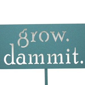 May include: A teal blue metal sign with the words "grow. dammit." in white lettering.