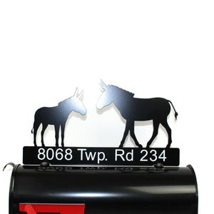 Puede incluir: Tope de buz&oacute;n de metal negro con dos siluetas de burro que se miran. El tope del buz&oacute;n tiene una placa de metal negro con la direcci&oacute;n "8068 Twp. Rd 234" en letras blancas.