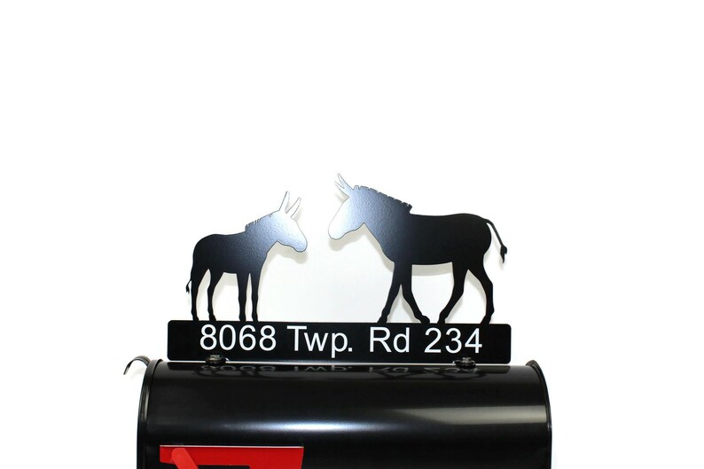 Puede incluir: Tope de buz&oacute;n de metal negro con dos siluetas de burro que se miran. El tope del buz&oacute;n tiene una placa de metal negro con la direcci&oacute;n "8068 Twp. Rd 234" en letras blancas.