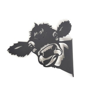 May include: Black metal silhouette of a cow's head with an open mouth, looking to the right. The cow's head is cut out of the metal and mounted on a black metal base.