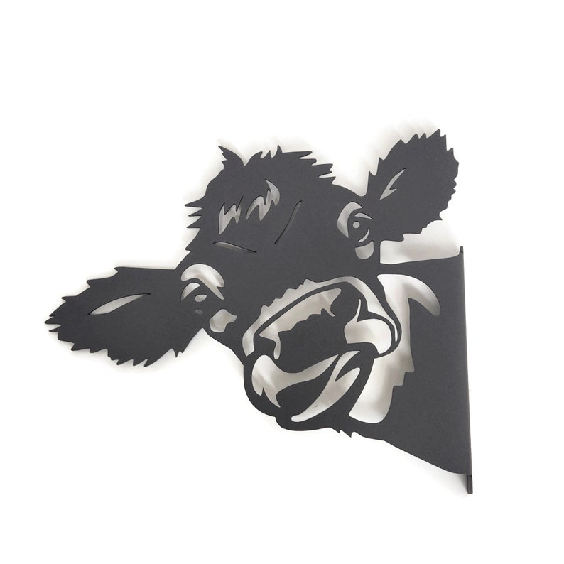 May include: Black metal silhouette of a cow's head with an open mouth, looking to the right. The cow's head is cut out of the metal and mounted on a black metal base.