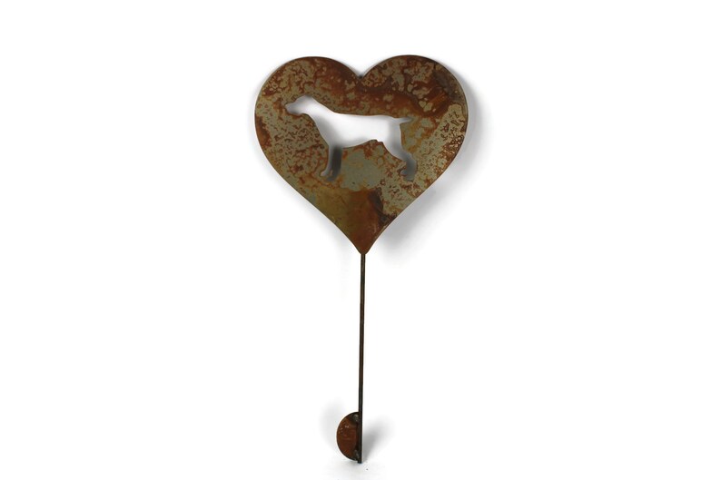 May include: A rustic metal garden stake featuring a heart shape with a dog silhouette cutout. The stake has a weathered, brown finish and a long stem with a small, rounded end. Ideal for adding a touch of charm to any garden or outdoor space.