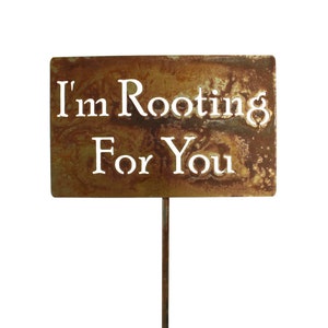 May include: A rusty metal sign with the words "I'm Rooting For You" in white lettering. The sign is attached to a metal stake.