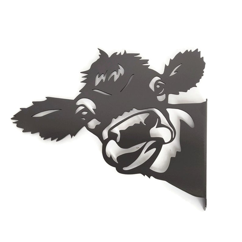 May include: Black metal wall decor featuring a cow's head with a playful expression. The cow's head is cut out of the metal, creating a silhouette effect.
