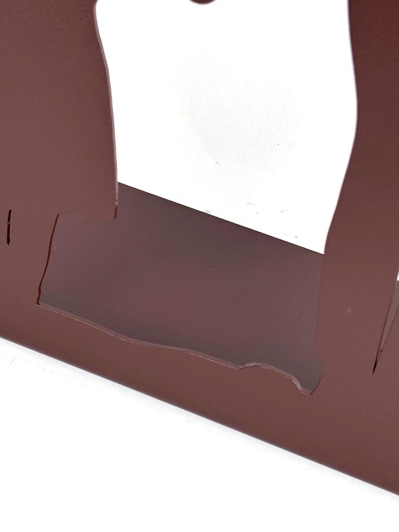 May include: A matte brown metal object featuring a flat base and two vertical, curved side panels that extend upward. The structure has a cutout design, creating a hollow center space between the two side elements, finished in a solid, uniform color.