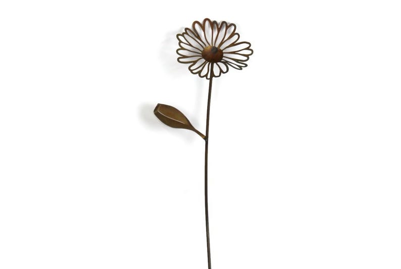 May include: A metal daisy garden stake with a brown stem, a flower head with a circular center, and a single leaf. The flower petals are outlined with thin metal lines. The garden stake is a decorative outdoor accent.