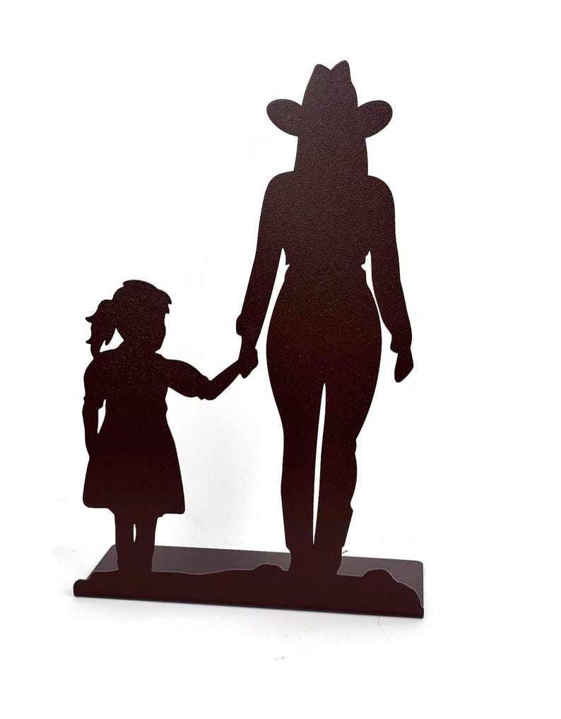 May include: A dark brown metal silhouette sculpture depicting a tall figure wearing a cowboy hat standing next to a smaller figure in a dress. The two figures are holding hands and are mounted on a flat, rectangular base of the same color.