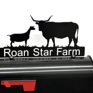 May include: Black metal mailbox topper featuring silhouettes of a goat and a longhorn steer above the words "Roan Star Farm" in white. The mailbox is black with a red flag.