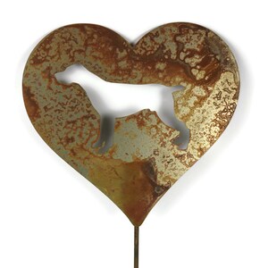 May include: A heart-shaped metal garden stake with a cut-out silhouette of a dog. The metal has a rustic, weathered appearance with shades of brown and gold. The stake is designed for outdoor use.