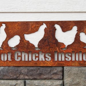 May include: Rusty metal sign with a cutout design of chickens and the text "Hot Chicks Inside".