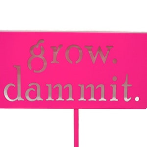 May include: A bright pink sign with the words "grow. dammit." in silver lettering.