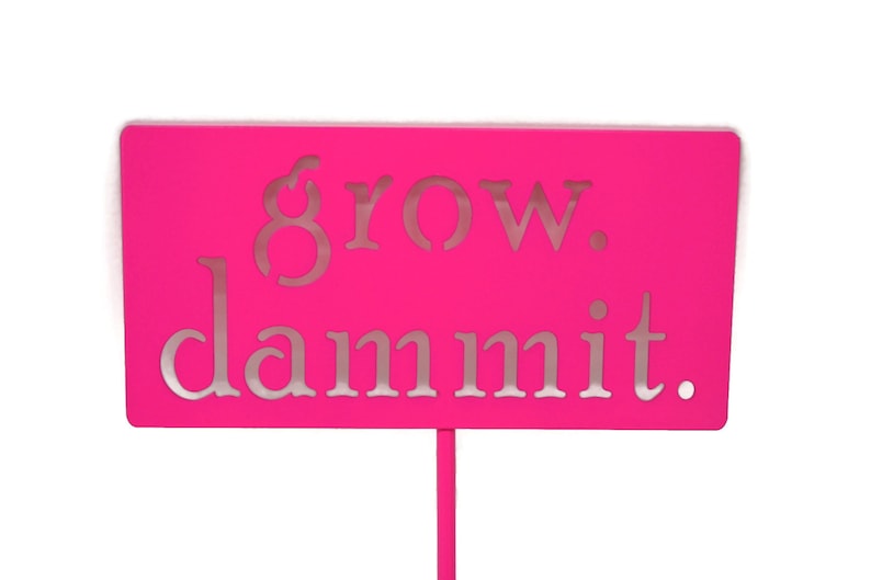May include: A bright pink sign with the words "grow. dammit." in silver lettering.